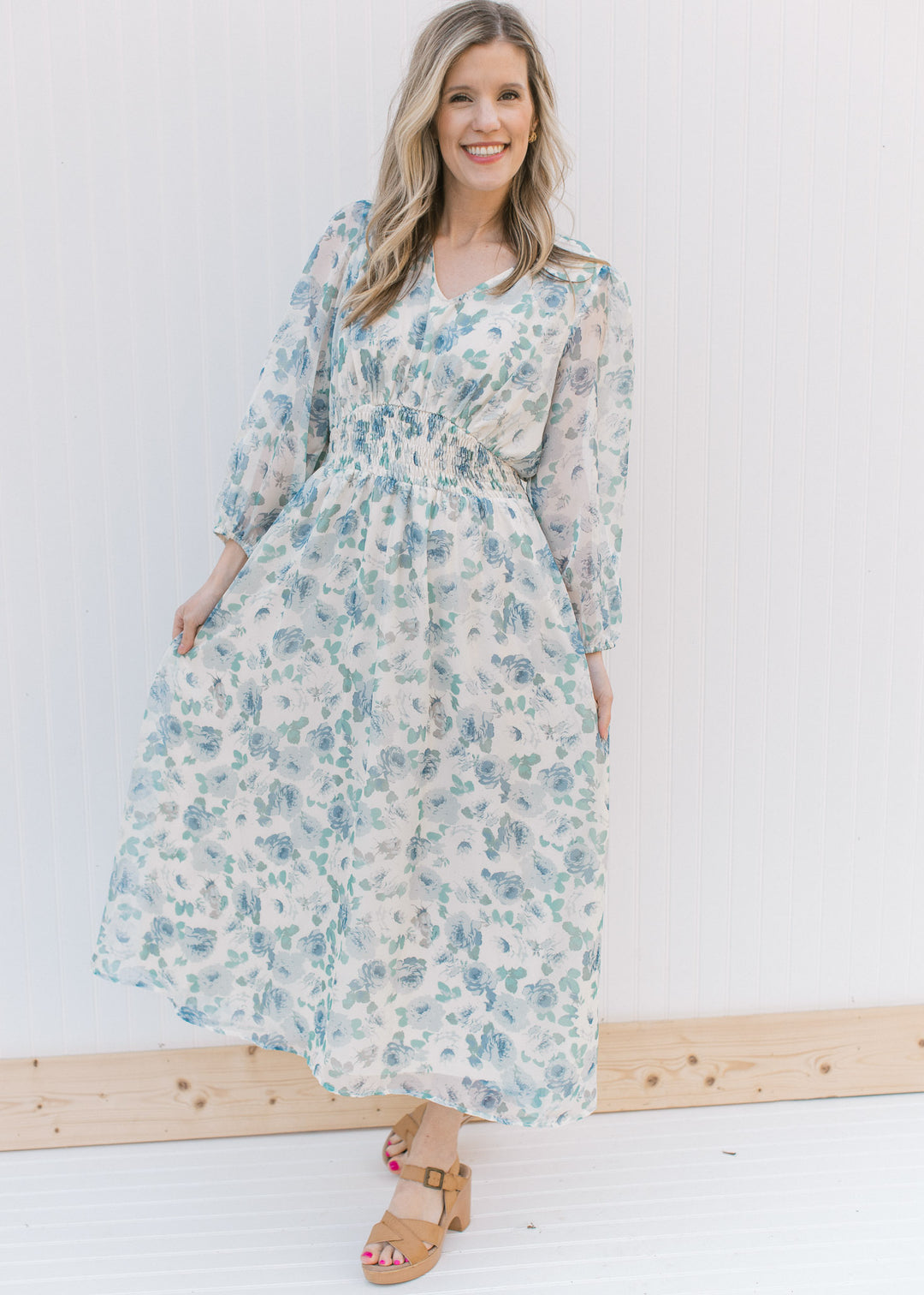 Model wearing heels with a cream midi with blue roses, an elastic waist and sheer 3/4 sleeves.