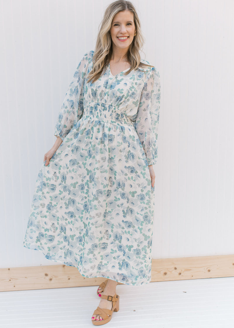 Model wearing heels with a cream midi with blue roses, an elastic waist and sheer 3/4 sleeves.