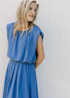 Side view of Model wearing a blue cropped balloon top with cap sleeves and pleated midi skirt. 