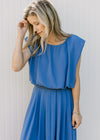 Close up of model in a blue, capped sleeve, balloon crop top with matching pleated midi skirt. 