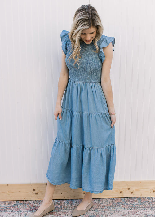 Model wearing a dusty blue midi with a smocked bodice, flutter cap sleeves and tiered skirt.