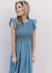 Close up of smocked bodice and flutter cap sleeves on a dusty blue midi with tiered skirt.
