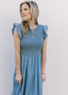 Close up of smocked bodice and flutter cap sleeves on a dusty blue midi with tiered skirt.