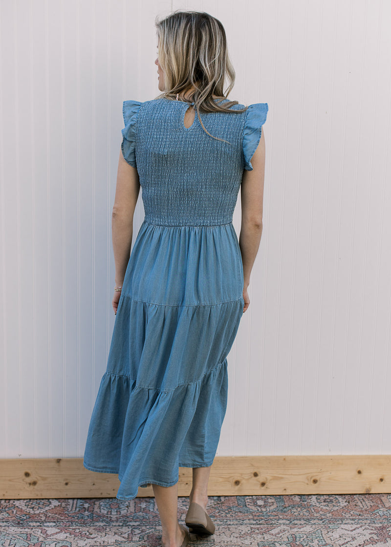 Back view of Model wearing a dusty blue midi with a smocked bodice and flutter cap sleeves. 