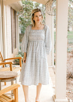 Model wearing heels and a cream midi with blue floral, square neckline and 3/4 bubble sleeves. 