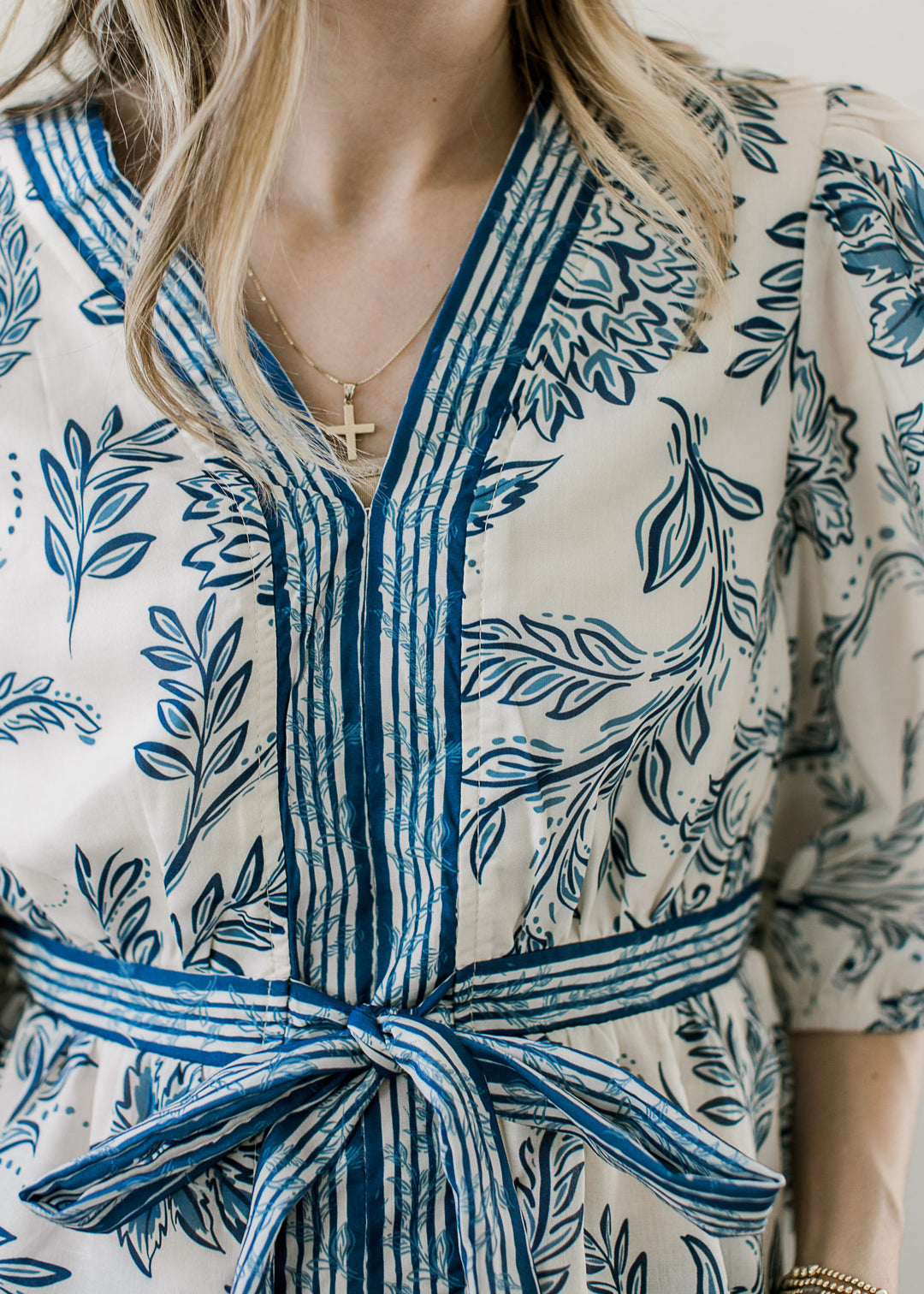 Close up of v-neck and blue striped detail at neck and waist on a cream top with blue floral. 