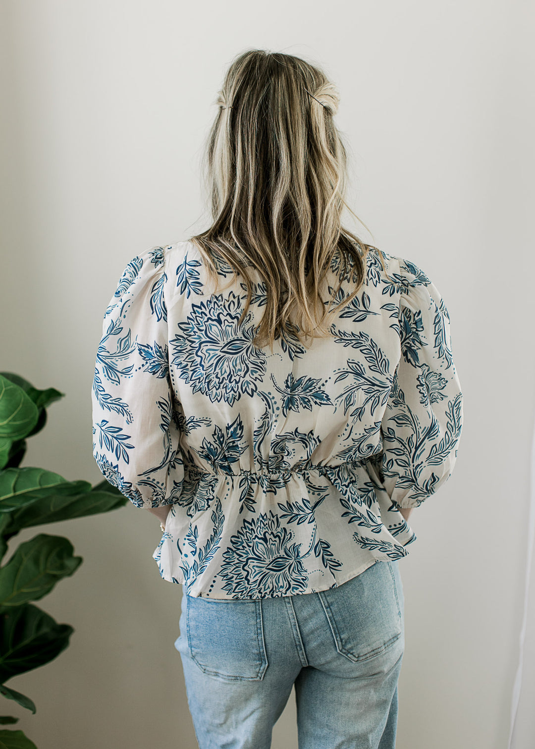 Back view of Model wearing a cream top with blue print 3/4 sleeves and elastic waist detail.
