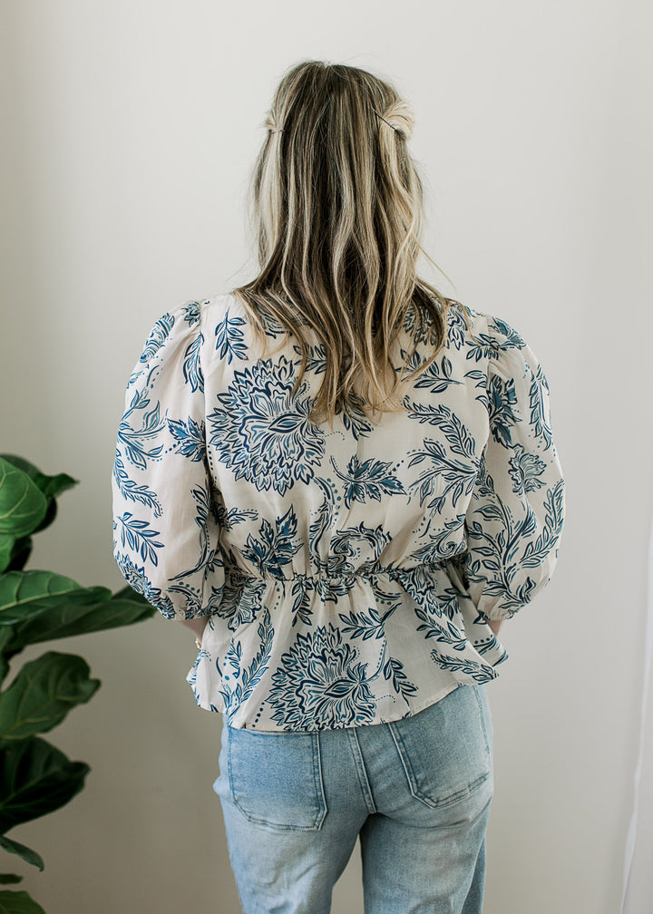 Back view of Model wearing a cream top with blue print 3/4 sleeves and elastic waist detail.