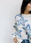 Close up of blue star pattern on a cream sweater with bubble long sleeves and a thick cozy material.