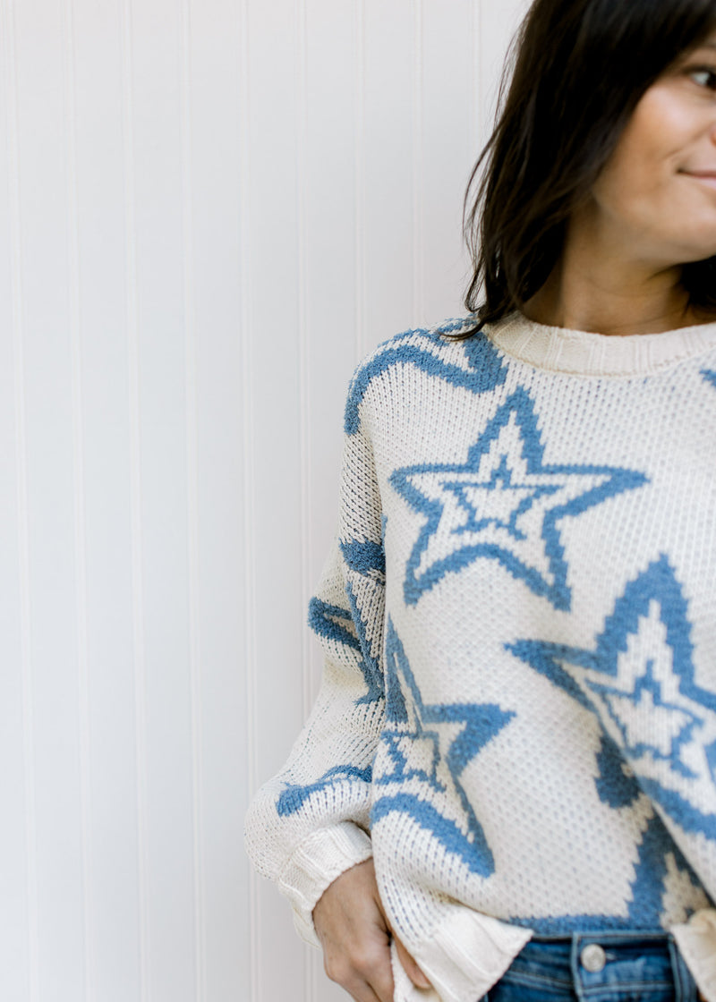 Close up of blue star pattern on a cream sweater with bubble long sleeves and a thick cozy material.