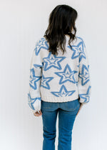 Back view of Model wearing a cream sweater with a blue star pattern and bubble long sleeves 