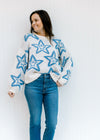 Model wearing jeans with a cream sweater with a blue star pattern, long sleeves and a round neck. 