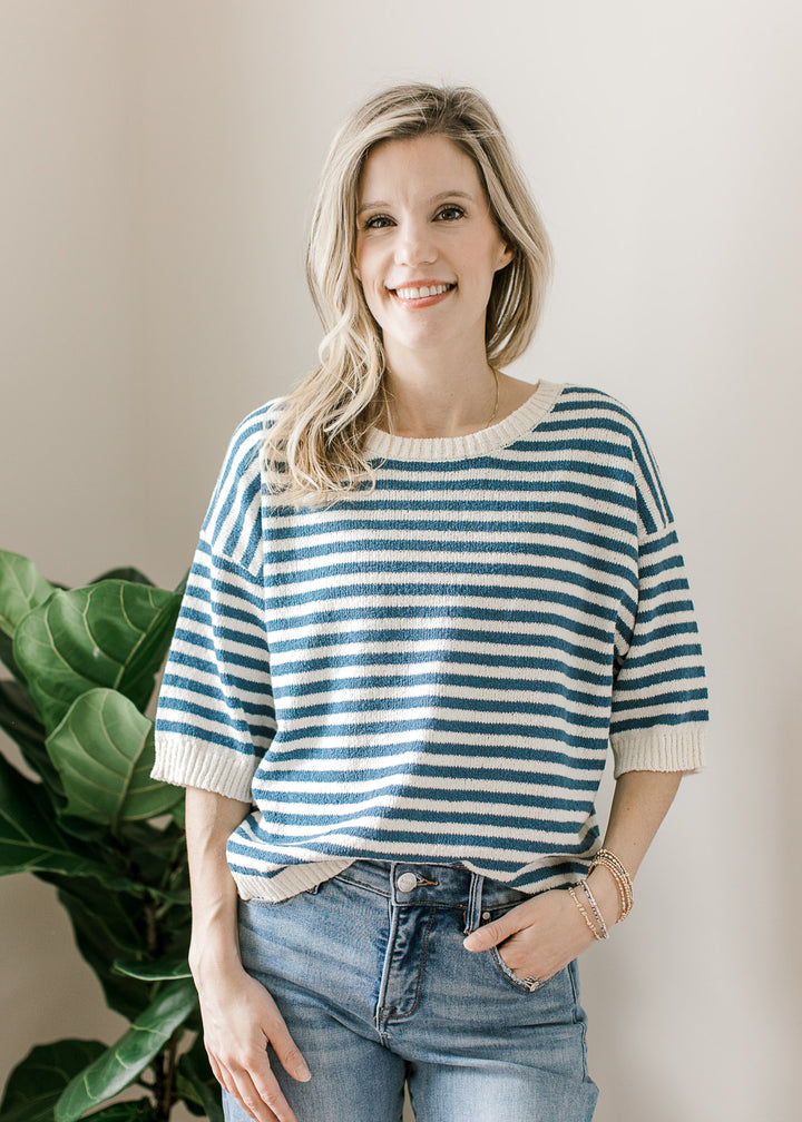 Model wearing a blue and cream striped knit sweater with short sleeves and button down the back. 