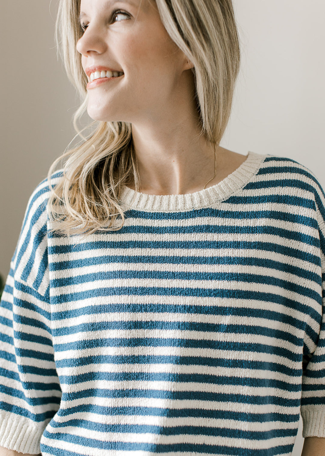 Close up of round neck with cream ribbed trim on a short sleeve blue and cream striped sweater. 