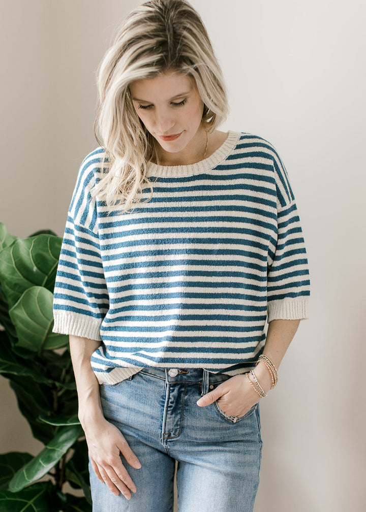 Model wearing a blue and cream striped knit sweater with short sleeves and cream ribbed trim. 