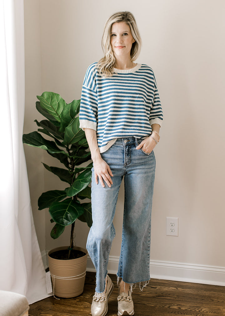 Model wearing jeans, mules and a blue and cream striped sweater with short sleeves.