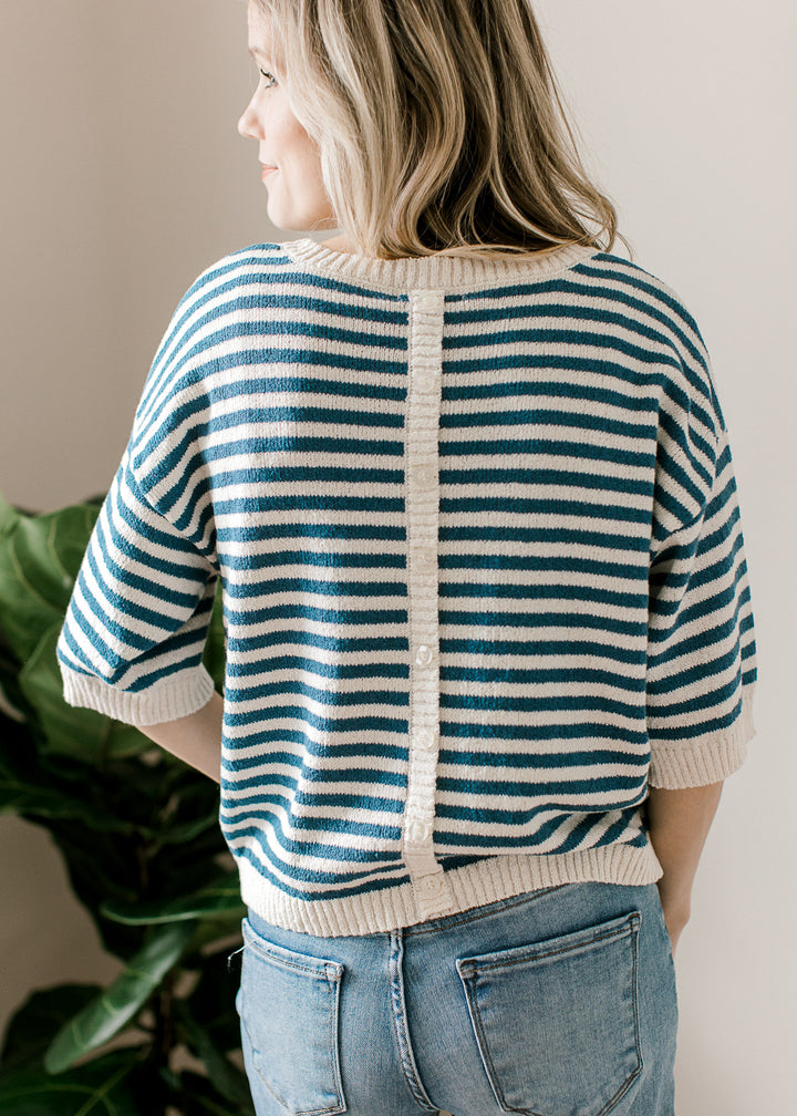 Back view of model wearing a blue and cream striped sweater with short sleeves and button on back. 