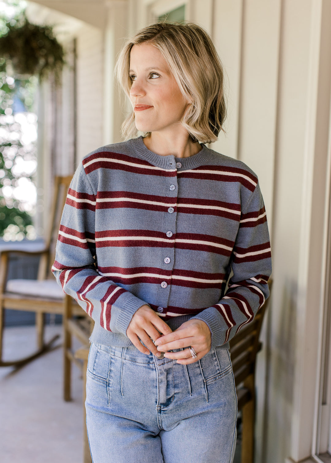 Model wearing a light blue cardigan with maroon and cream stripes, buttons and long sleeves. 
