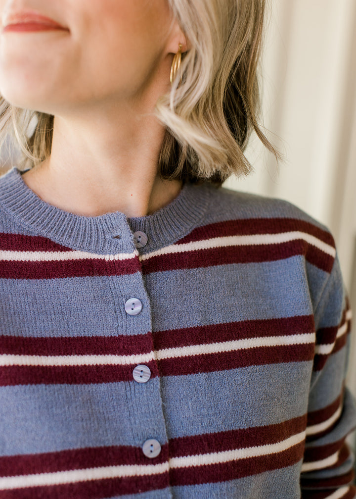 Close up of buttons and ribbed detailing along the rounds neckline of a blue cardi with stripes. 