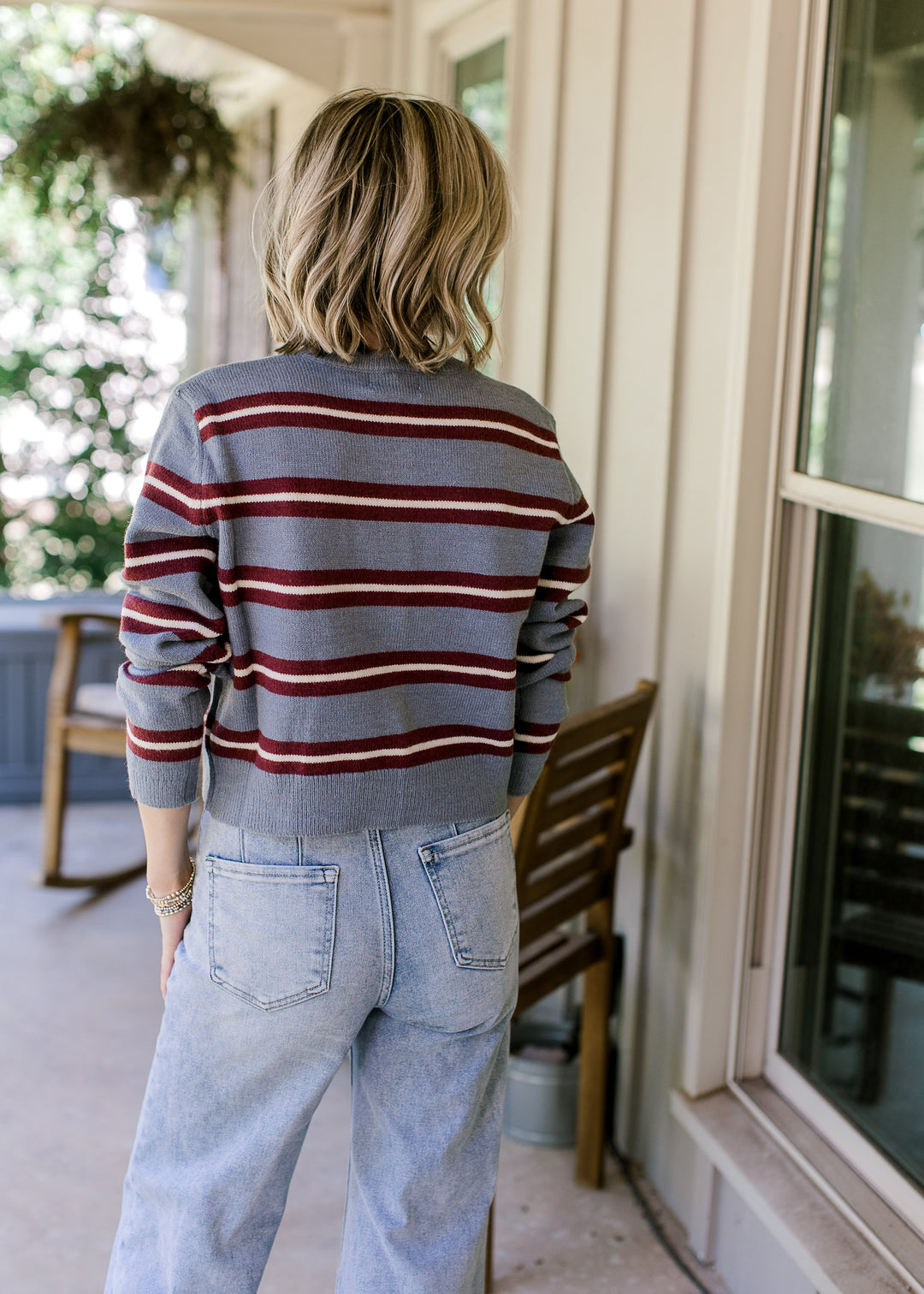 Back view of Model wearing a blue cardigan with maroon and cream stripes, buttons and long sleeves. 