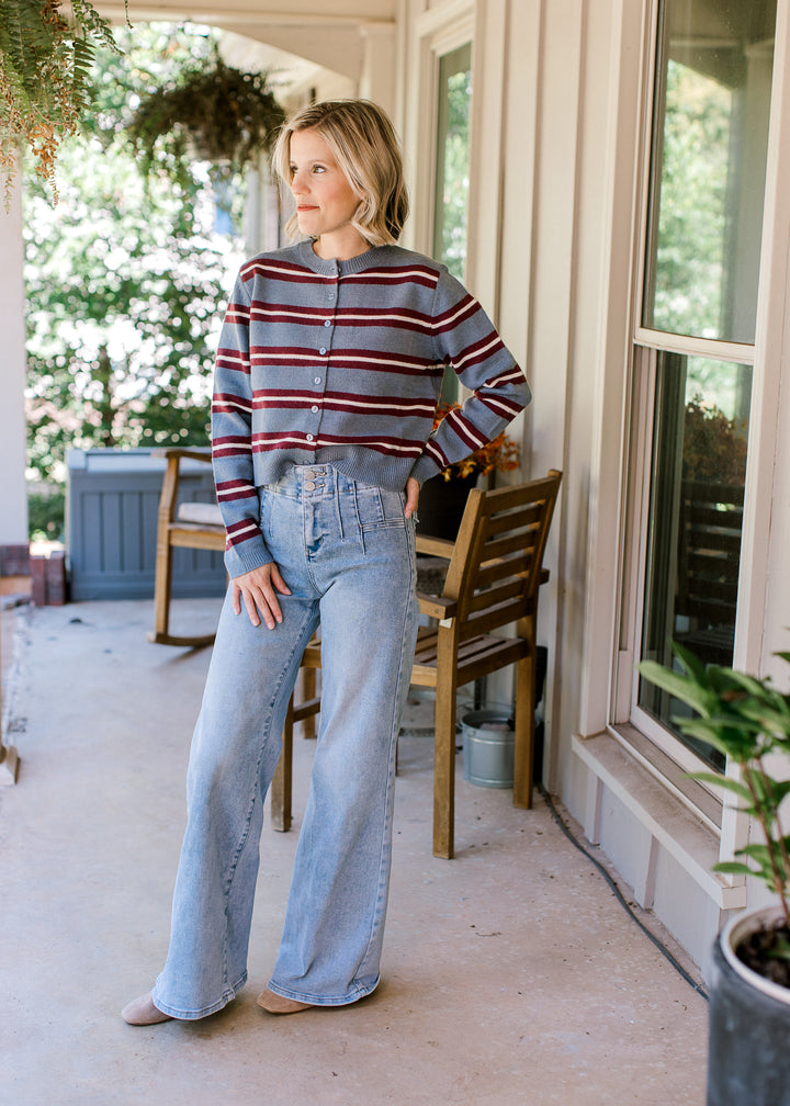 Model wearing jeans, boot and a light blue long sleeve cardigan with maroon and cream stripes. 