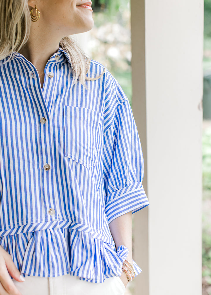 Close up of button and patch pocket on a short sleeve blue and white striped top with a collar.