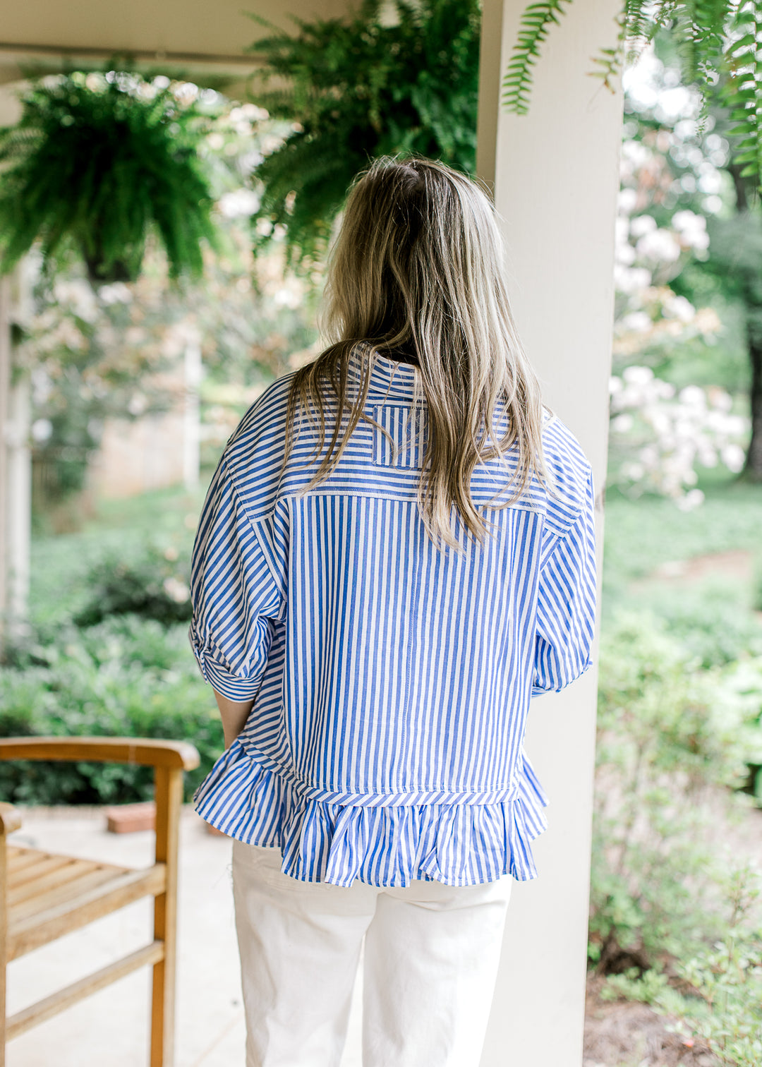 Back view of Model wearing a short sleeve blue and white striped top with a collar and ruffle hem.