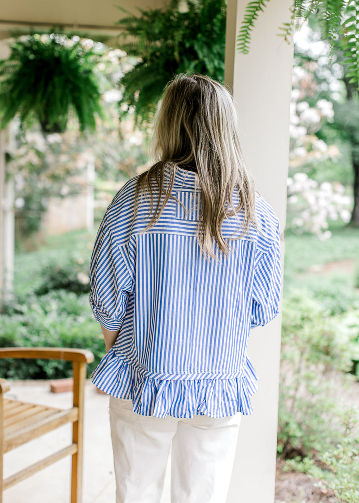 Back view of Model wearing a short sleeve blue and white striped top with a collar and ruffle hem.