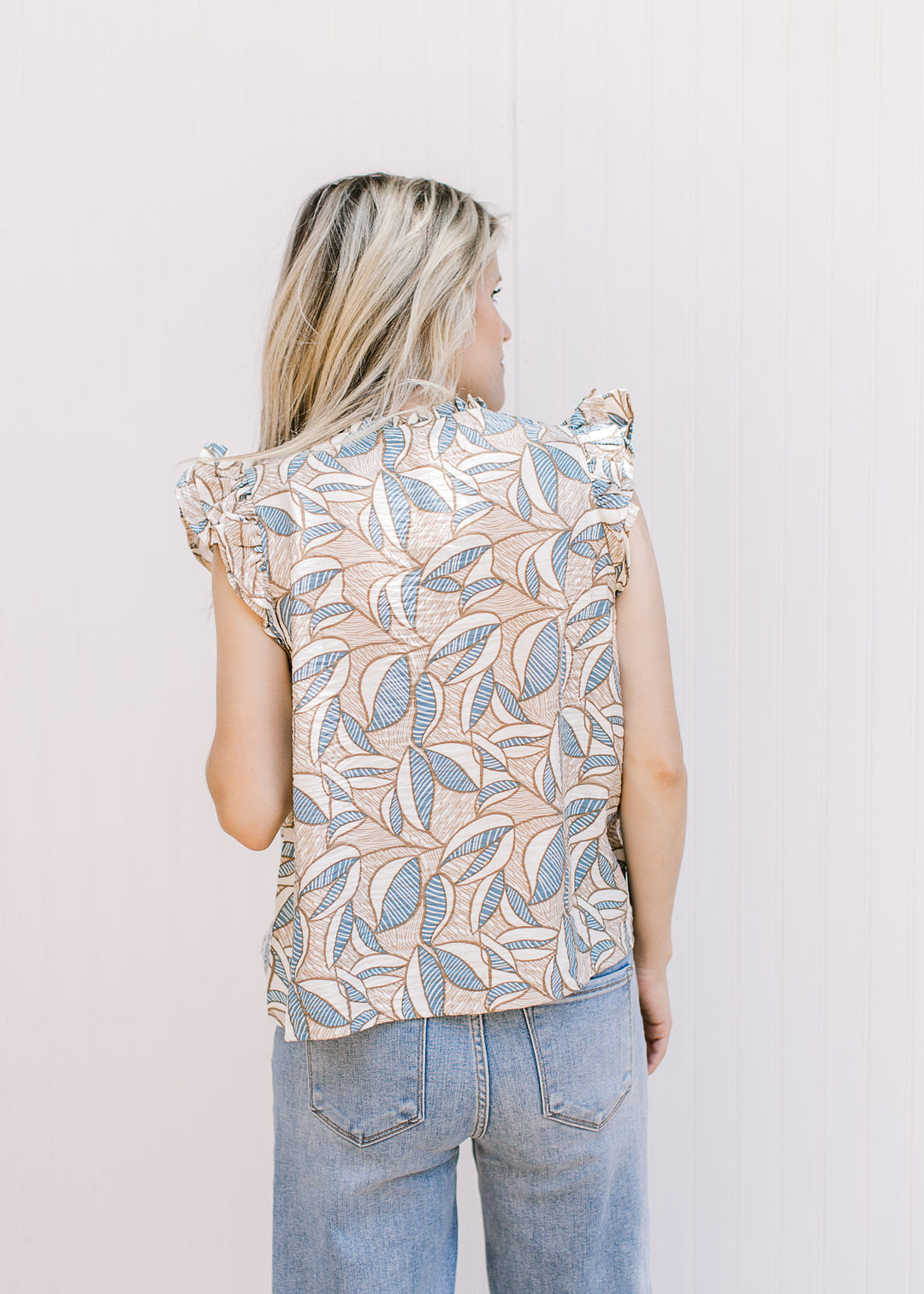 Back view of model wearing a tan top with cream and blue pattern and flutter cap sleeves. 