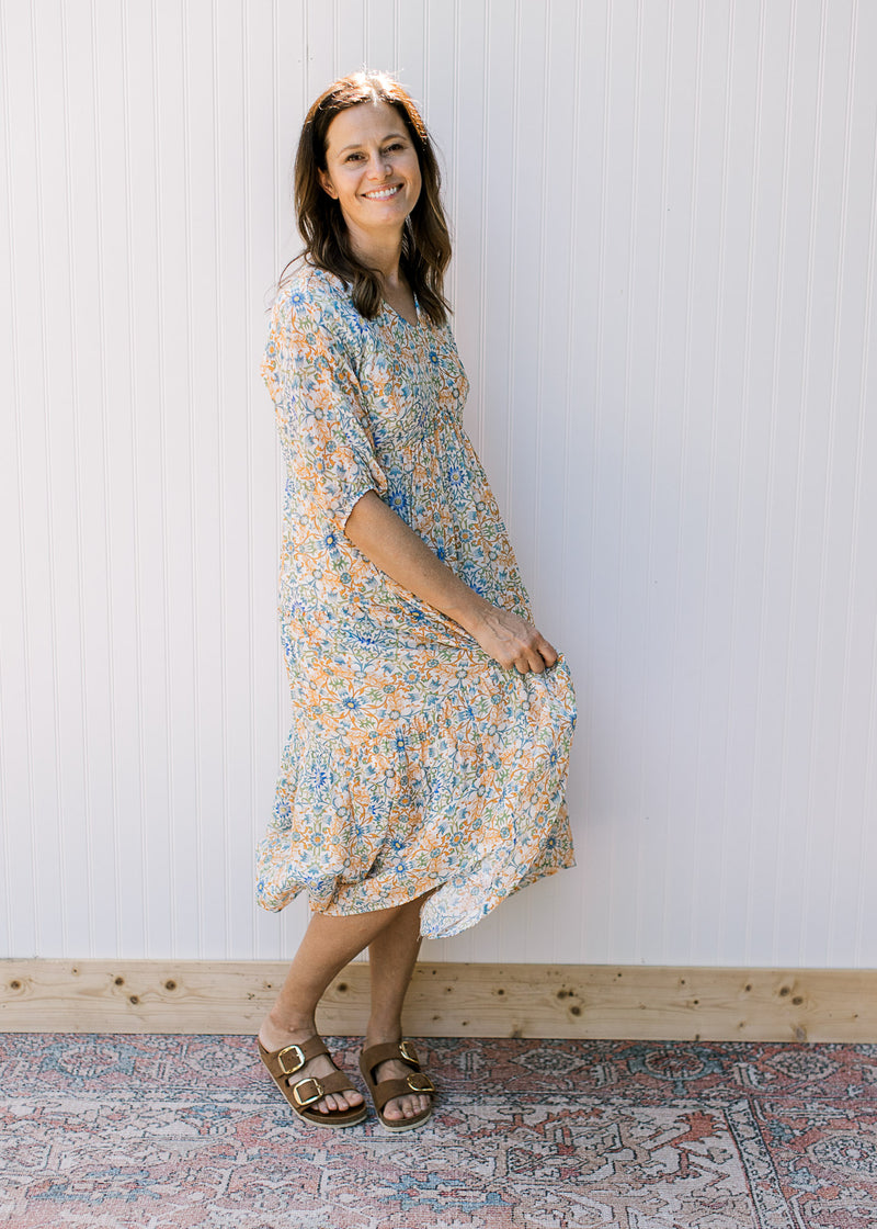 Model wearing a cream midi with blue, green and orange flowers and 3/4 sleeves. 