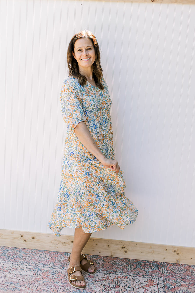 Model wearing a cream with blue, green and orange flowers and 3/4 sleeves. 