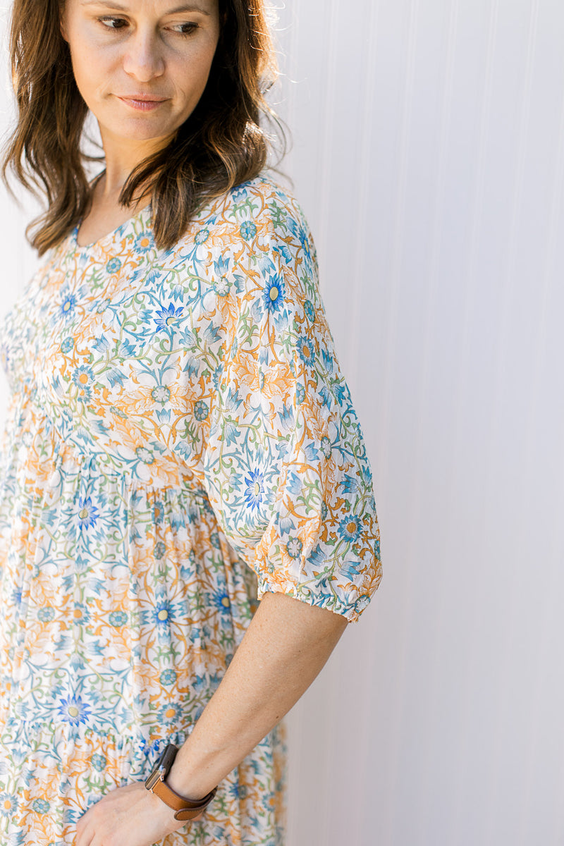 Close up of 3/4 sleeve with elastic band on a cream dress with orange, blue and green flowers.