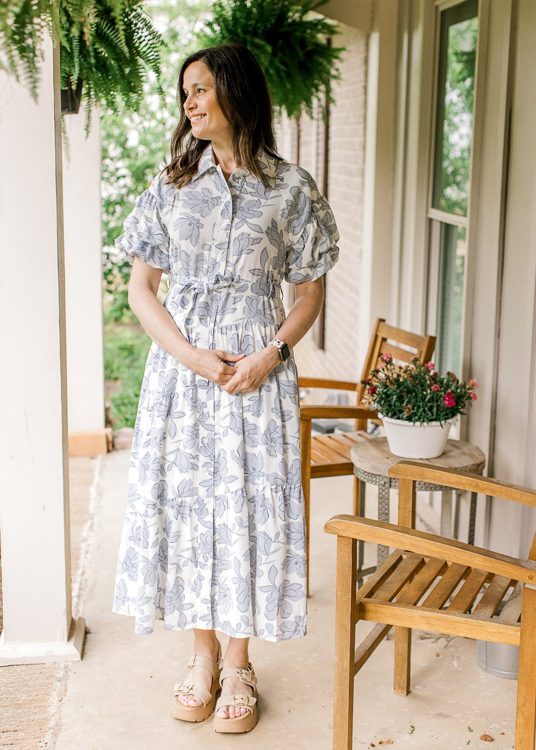 Model wearing a cream button up dress with gray blue flowers, bubble short sleeves and a tie.