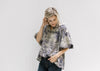 Model wearing a tan v-neck top with navy toile print, bubble short sleeves and ruched neck detail. 