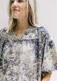 Close up of navy toile print on a tan top with a ruched v-neck and bubble short sleeves. 