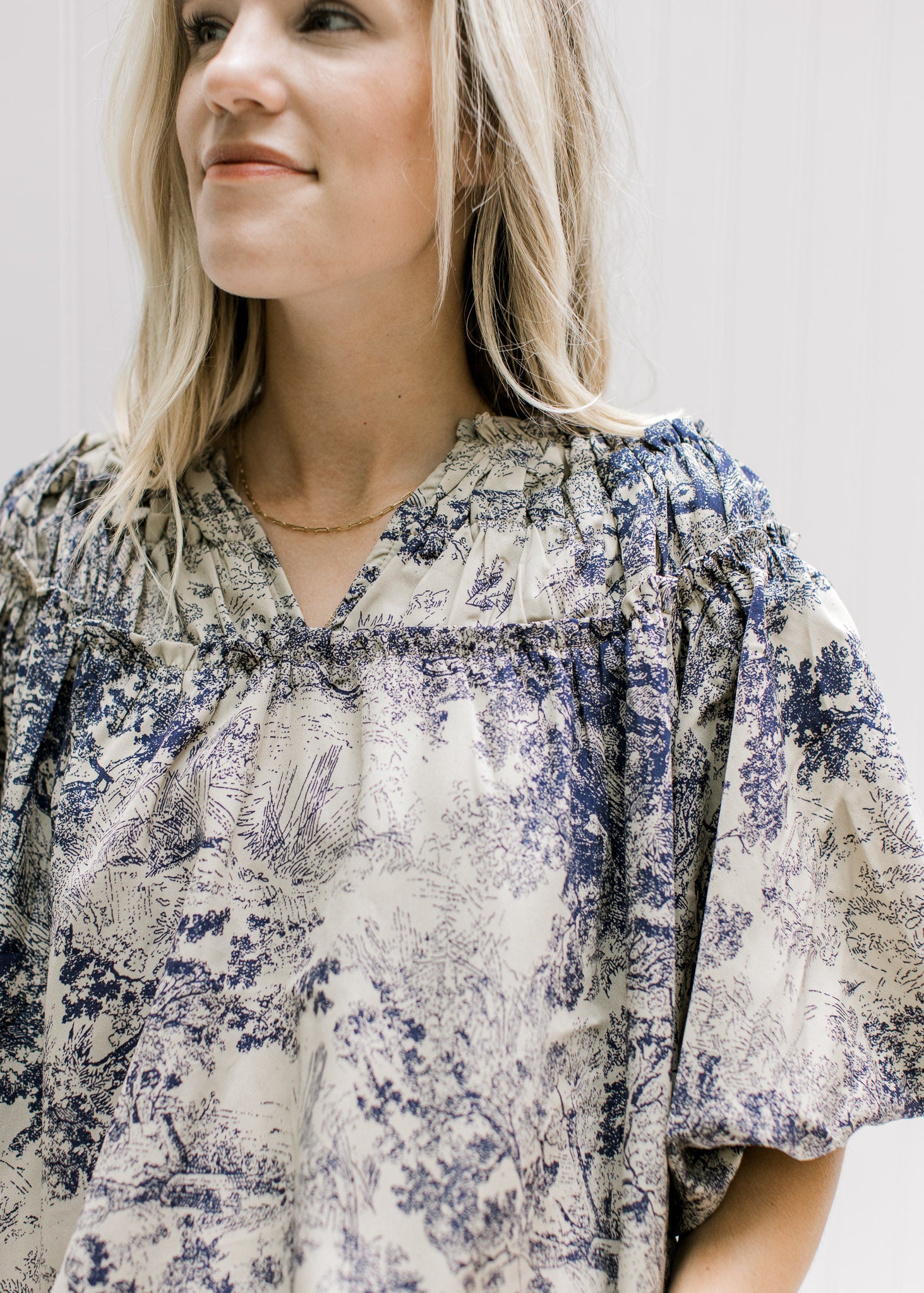 Close up of navy toile print on a tan top with a ruched v-neck and bubble short sleeves. 