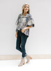 Model wearing jeans and booties with a tan top with navy toile print and bubble short sleeves. 