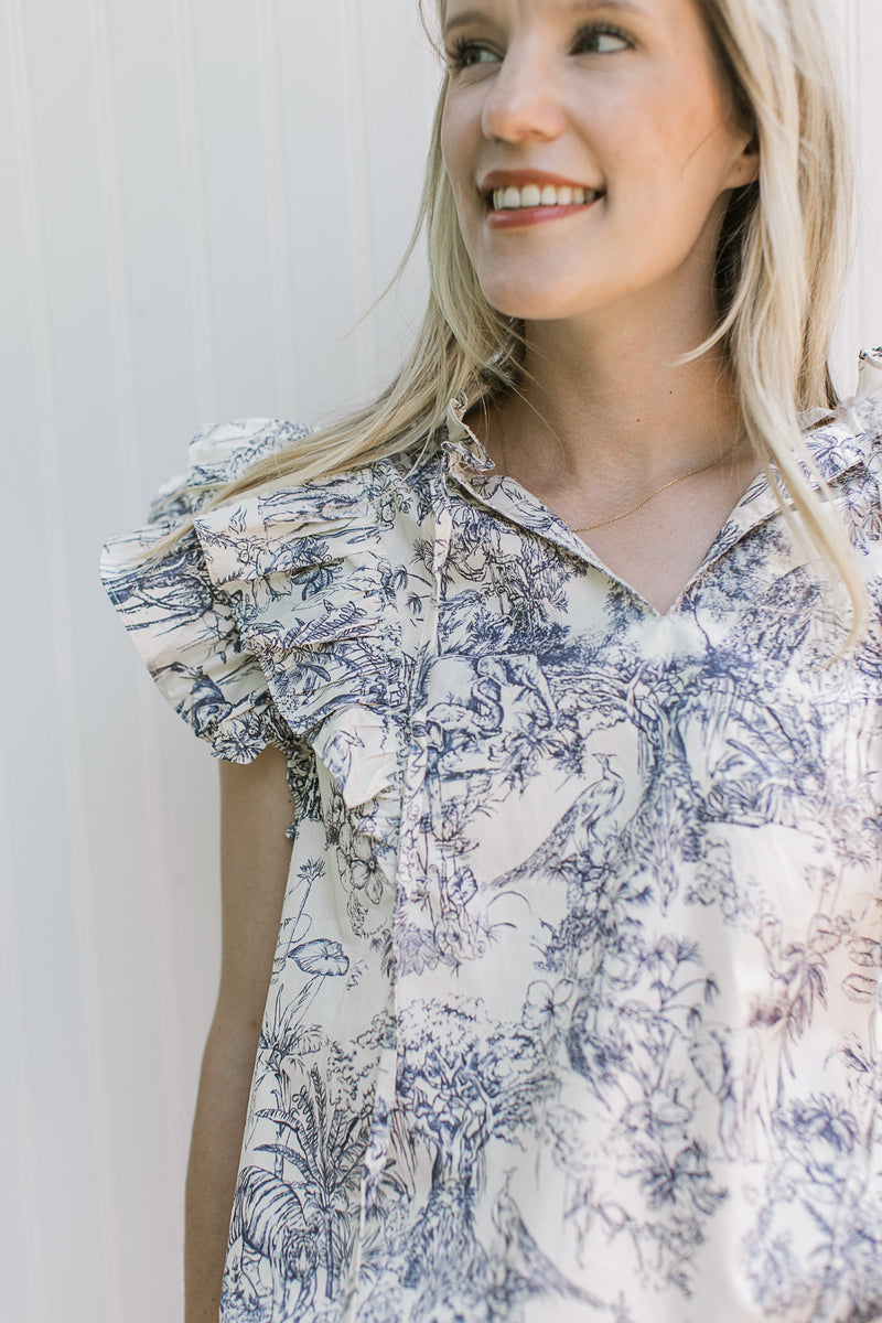 Close up of a model wearing a blue toile top, a v-neck with a tie and layered ruffle sleeves. 