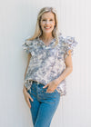 Model wearing a blue toile top with layered ruffle cap sleeves and a v-neck.