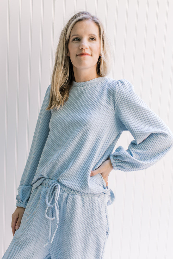 Model wearing a lightweight blue waffle grid top with a round neck and bubble long sleeves. 