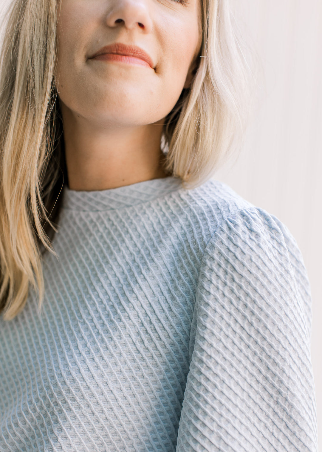 Close up view of pleating on the shoulder of a light blue waffle grid top with a round neck. 