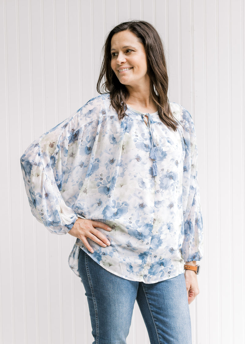 Model wearing a white top with a blue floral watercolor print and long sleeves with elastic cuff. 