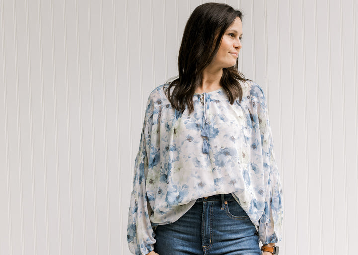 Model wearing a white top with a blue floral watercolor print and a v-neck with a tie closure. 