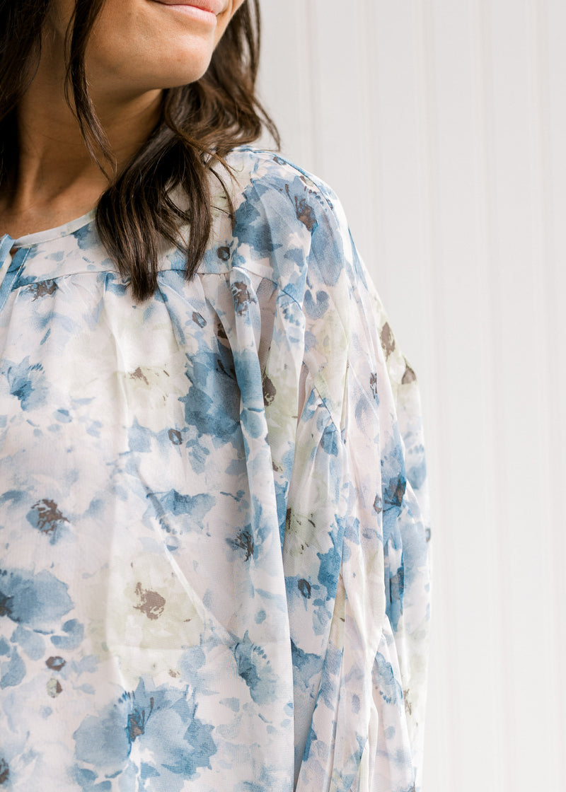 Close up view of sheer sleeves on model wearing a white top with a blue floral watercolor print. 