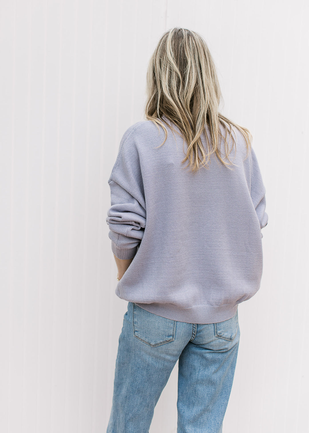 Back view of Model wearing a purplish-blue sweater with a whale graphic and long sleeves. 