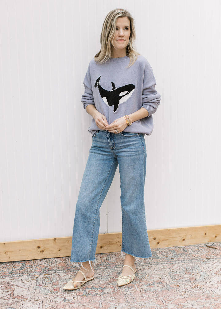 Model wearing jeans, flats and a purplish-blue sweater with a whale graphic and long sleeves. 