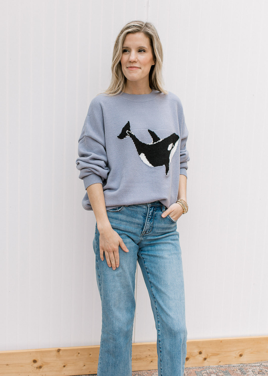 Model wearing a soft purplish-blue sweater with a whale graphic, round neck and long sleeves. 