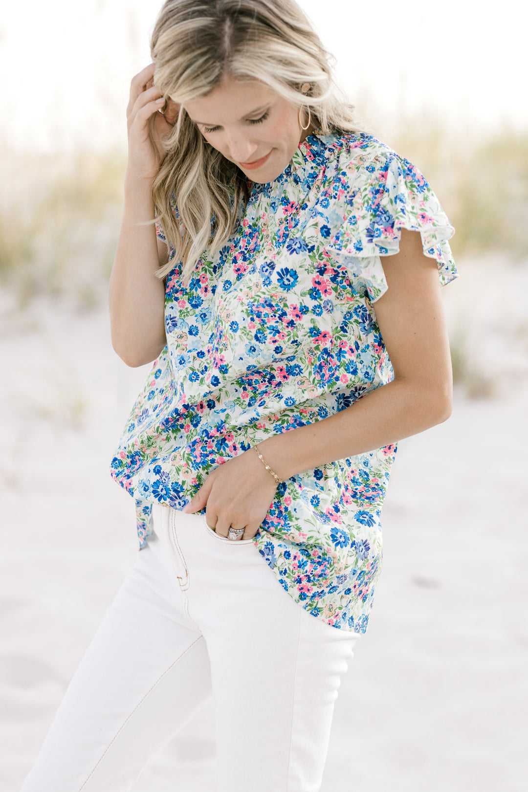 Model wearing a white top with a blue floral pattern, ruffle mock neck, cap sleeves and keyhole. 
