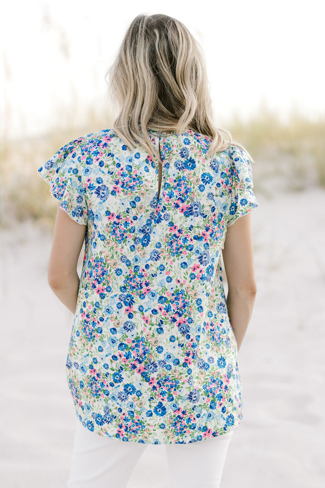 Back view of a model wearing a white top with a blue flora pattern and a keyhole closure. 