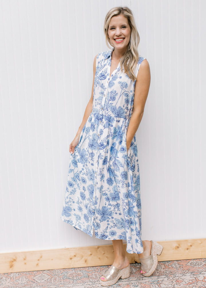 Model wearing a fully lined white dress with blue floral, pockets, button front and a collar.